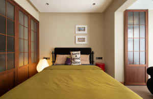 A minimalist bedroom with a yellow bed, black and white pillows, and a black headboard.