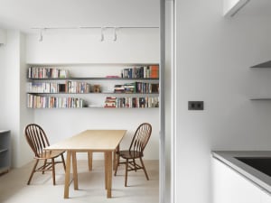 Minimalist dining room featuring a wooden table, wooden chairs, and a metal bookshelf filled with books.