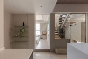 Modern minimalist residential space with a glass staircase, stone floor, and wooden elements.