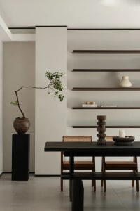 Minimalist dining room featuring a black table, wooden chairs, and ceramic plant pot with greenery.