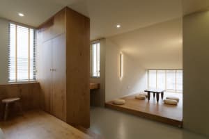 A minimalist living space featuring wooden furniture and flooring, with a low table and cushions for seating.