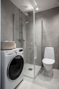 Modern bathroom with concrete walls, glass shower enclosure, washing machine, and toilet.