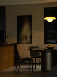 A minimalist dining room featuring black leather chairs and a round table with a bowl of fruit.