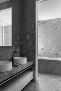 A modern bathroom featuring granite walls and marble sinks.