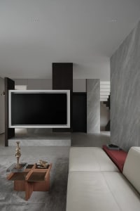 A modern living room with a white leather sofa, a marble coffee table, and a large television screen mounted on a marble colu
