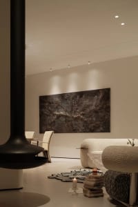 A modern living room with mixed materials, featuring a black fireplace, abstract art, and plush furniture.