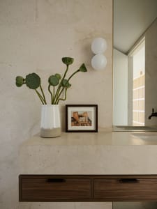 A minimalist bathroom featuring a white vase with green lotus pods and a framed painting of buildings in the background.