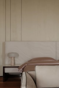 A minimalist bedroom featuring a beige upholstered bed with marble nightstand and beige fabric bedding.