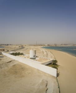 Modern beach-front property with a cylindrical concrete structure on a sandy beach.