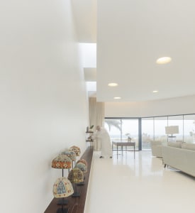 Spacious, minimalist living room featuring concrete flooring and walls, with large windows overlooking the ocean.