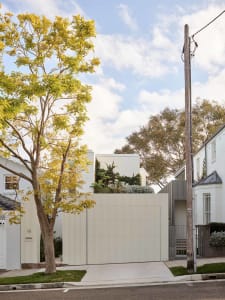 Modern minimalist metallic residential exterior with a white fence and a tree in the foreground.