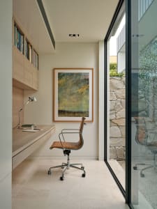A modern office space featuring a wooden desk, glass window, and abstract painting.