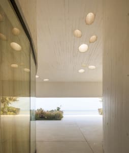 A modern interior design featuring a concrete entrance hall with ocean views and spherical light fixtures.
