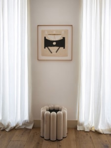 A modern room setting with white curtains and a white side table with a black base.