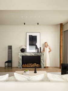 A minimalist living room with a marble fireplace, black furniture, and contemporary decor.