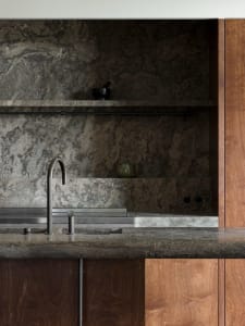 A modern kitchen interior featuring a granite countertop and backsplash, with a metal faucet and wooden cabinets.