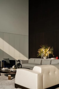 A modern living room with neutral textiles, including a beige sofa, dark armchair, and a wooden coffee table.