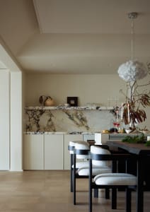 A minimalist dining room featuring a marble counter, white chairs, and a modern light fixture.
