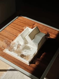 A modern house model made of plastic, featuring a unique architectural design with a central courtyard, surrounded by trees a