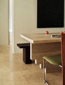 A modern interior space featuring a concrete table with a dark wooden bench and a green upholstered chair.