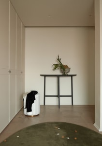 A minimalist entryway with neutral-toned walls, a wooden table, and a green rug with small white dots.