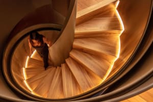 Person walking up a spiraling wooden staircase illuminated by LED lights at night.