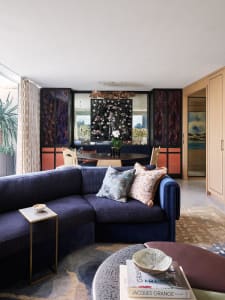 A modern living room with a navy blue sofa, patterned rug, and abstract art on the wall.