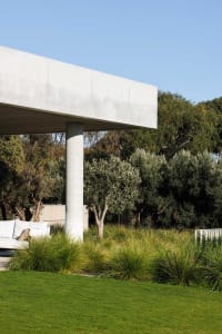 Minimalist architectural design with concrete structure, green grass, and planted trees outdoors.