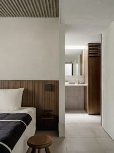 Modern bedroom with minimalist design featuring wood paneling on the headboard and walls, concrete floor, and white walls.