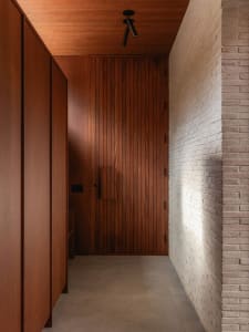 A modern minimalist entrance hall featuring a wooden door, concrete floor, and brick wall.