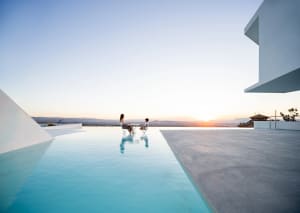 A modern vacation home with a glass infinity pool at sunset.