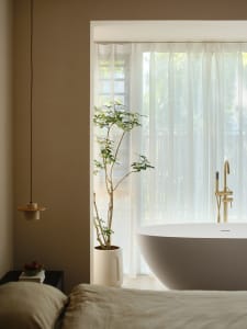 A minimalist bedroom featuring a white bathtub, sheer white curtains, and light-colored fabric bedding.