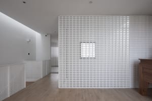 Minimalist white room with grid-patterned walls and ceiling, featuring a wooden floor and a fireplace.