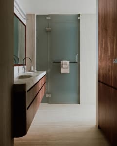Modern bathroom with glass shower enclosure, wooden cabinets, and white marble countertop.