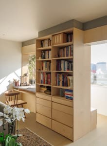 A modern home office featuring wooden shelves filled with books and storage drawers below.