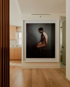 A minimalist interior photograph featuring a female model seated on a stool.