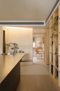 Modern minimalist kitchen with wooden cabinets and countertops, featuring an orange chair and green plants.