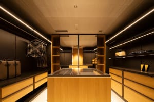 Modern closet with wooden shelves and mirrored doors, featuring a central island with a glass top.