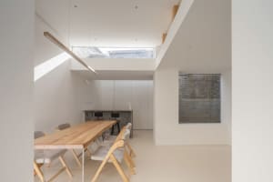 Modern kitchen and dining area with wooden table and chairs, light-colored walls, and floor-to-ceiling windows.
