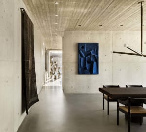 A modern interior space featuring a concrete wall, a blue abstract sculpture, and a wooden dining table with chairs.