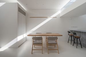 A minimalist dining area with wooden furniture and concrete flooring, featuring a long wooden table and gray upholstered chai