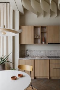 A modern kitchen with wooden countertops and cabinets, featuring a round table, bowls, and potted plant.