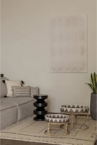 Modern interior design featuring a gray couch, black acrylic artwork, black and white patterned bamboo side tables, and a woo