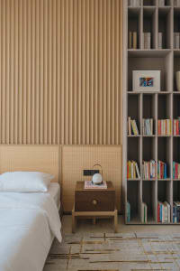 A modern minimalist bedroom featuring a bed with a wooden headboard, a wooden nightstand, and a large bookshelf filled with b