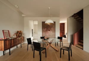 A modern dining room featuring black chairs and a round glass table with wooden legs.