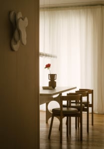 A minimalist dining room with wooden furniture and a single red flower in a vase.