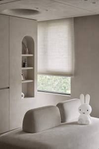 A modern minimalist living room with a grey sofa, a white rabbit-shaped lamp, and a window with blinds.