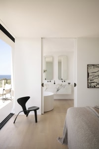A modern residential interior featuring a marble bathroom with a round bathtub, double vanity, and floor-to-ceiling windows.