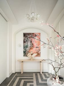 A modern entryway with a minimalist design, featuring a concrete floor and a table with a vase and abstract painting.