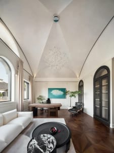 A spacious modern home office with a large white sofa, a black and white marble coffee table, a wooden desk, and a black loun